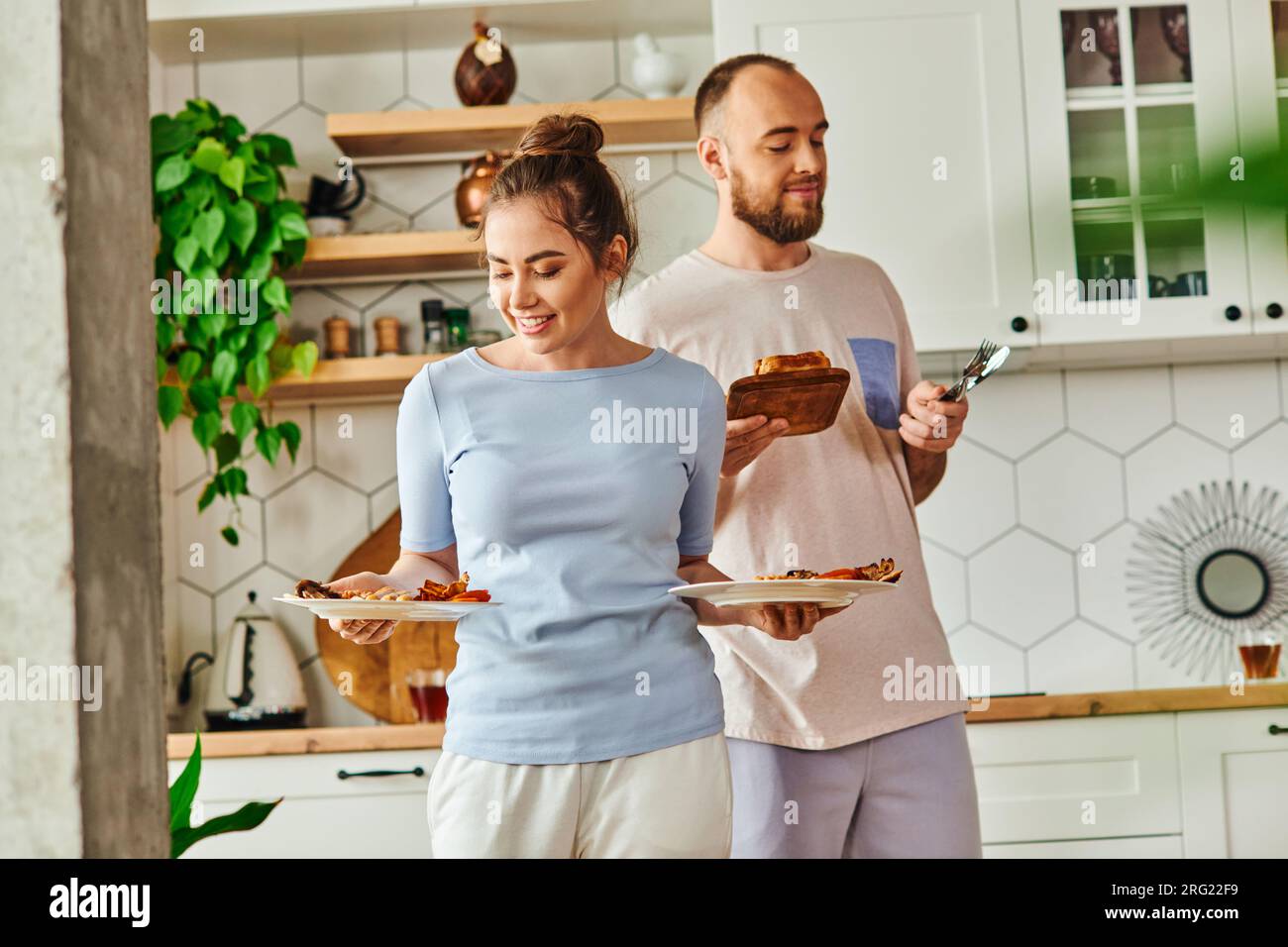 Femme positive tenant le petit déjeuner près de petit ami avec des couverts et du pain à la maison le matin Banque D'Images