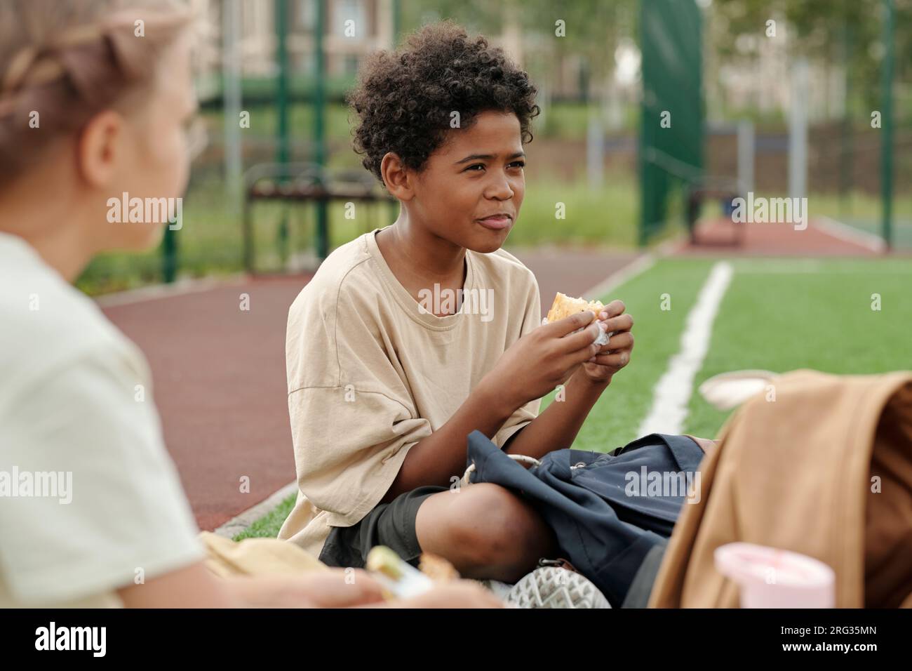 Mignon garçon afro-américain affamé en vêtements décontractés mangeant un  sandwich ou une autre collation pour le déjeuner tout en étant assis parmi  ses camarades de classe ou amis Photo Stock - Alamy