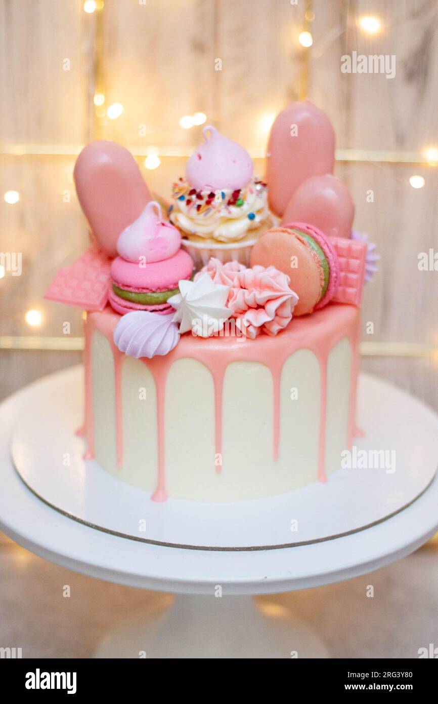Beau gâteau décoré de chocolat rose fondu, macarons, meringues, cake POPS et bonbons sur fond festif Banque D'Images