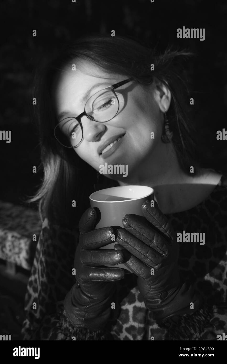 Portrait noir et blanc de femme souriante aux yeux fermés. Femme mature dans la lumière du soleil du matin avec tasse à café, noir et blanc. Le concept d'estime de soi. Banque D'Images