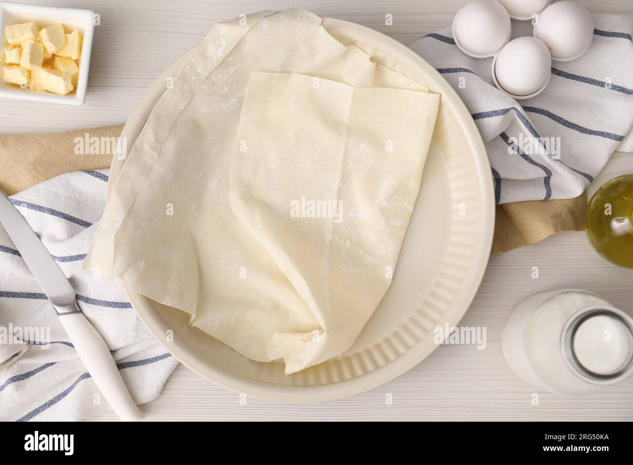 Pâte fraîche et différents ingrédients pour faire du baklava sur table en bois blanc, pose à plat Banque D'Images