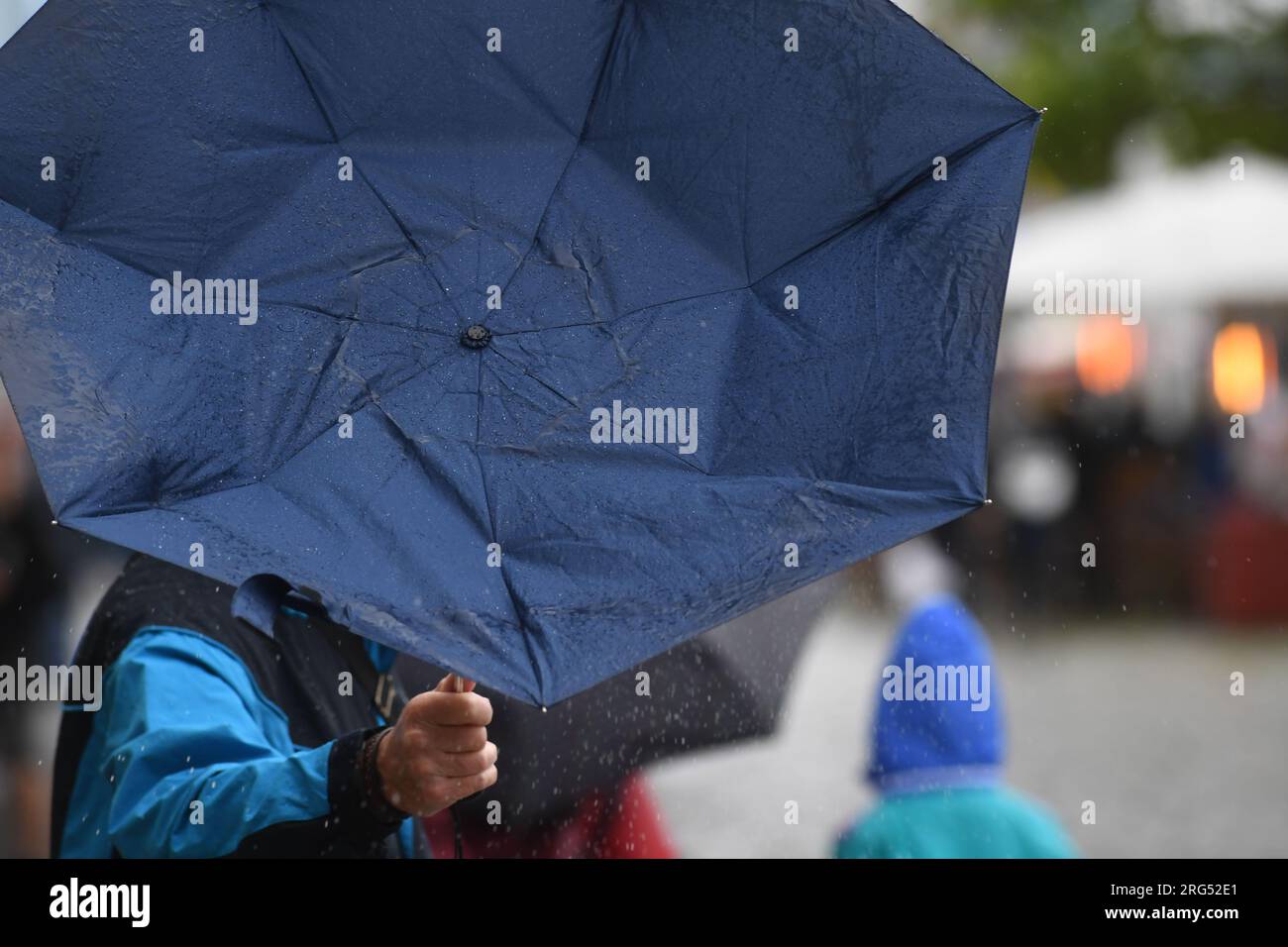 Stralsund, Allemagne. 07 août 2023. Un homme avec un parapluie endommagé  marche dans le port de Stralsund. Les météorologues s'attendent à des  conditions météorologiques changeantes en mer Baltique également dans les  prochains