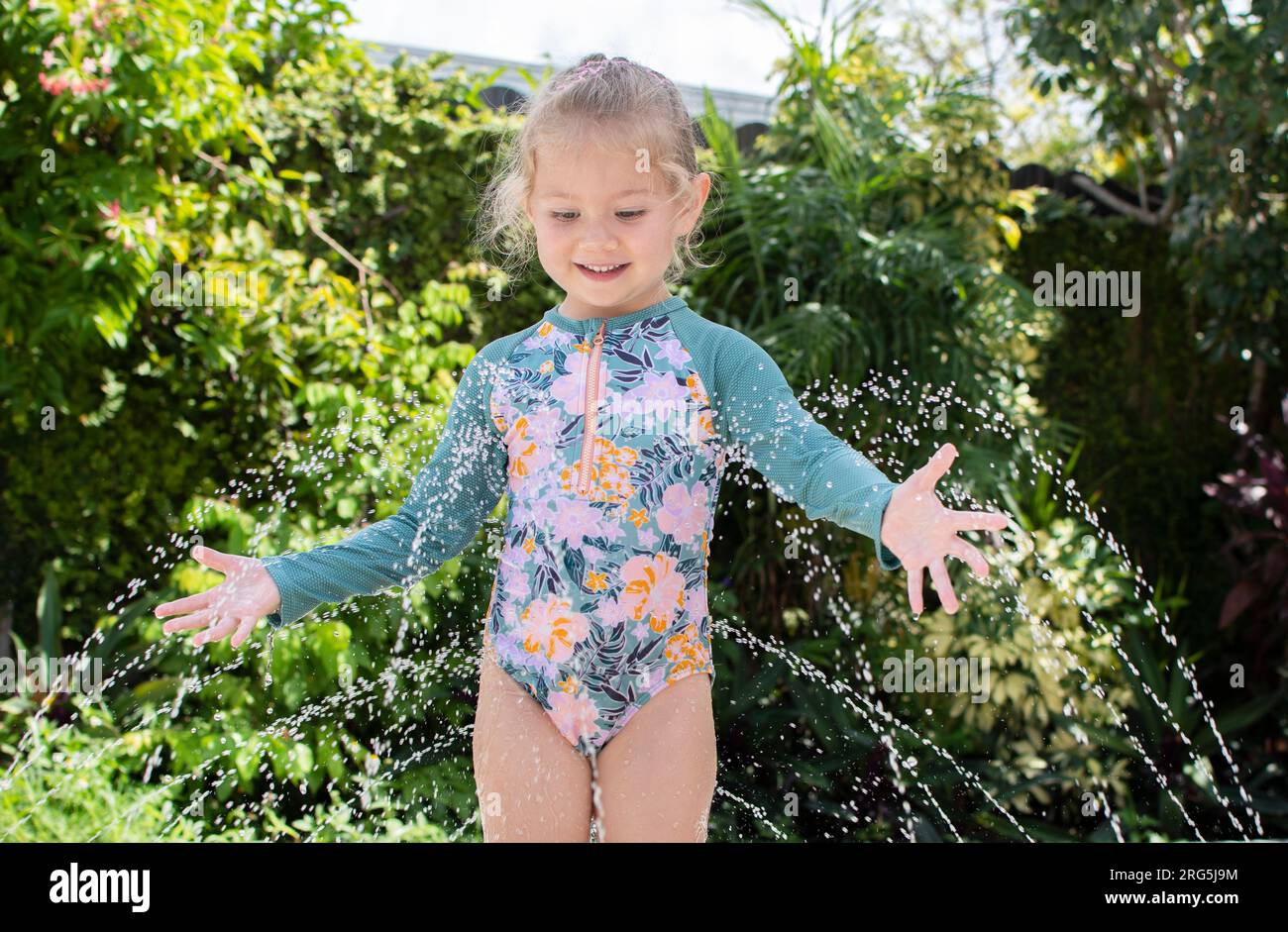 Mignonne petite fille caucasienne joue avec l'eau Oh un jour d'été. Concept d'activités estivales amusantes pour les enfants. Tampon anti-éclaboussures Banque D'Images