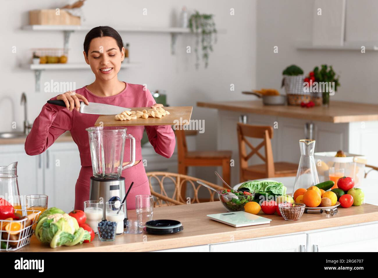 Jeune femme sportive mettant la banane coupée dans le mélangeur dans la cuisine Banque D'Images