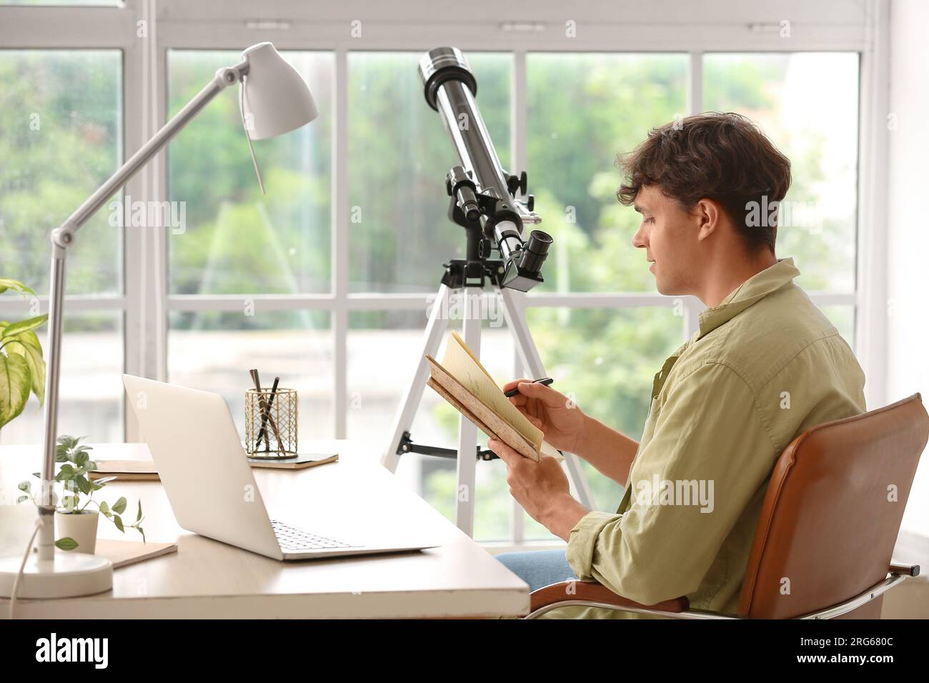Jeune homme avec télescope et cahier à table Banque D'Images