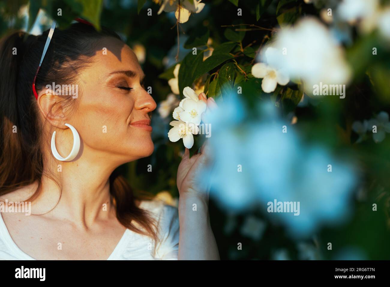 Heure d'été. femme élégante souriante en chemise blanche près de l'arbre à fleurs. Banque D'Images