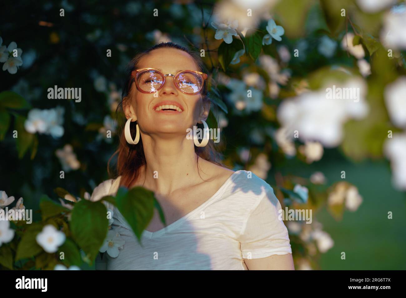 Heure d'été. heureuse femme d'âge moyen élégante en chemise blanche avec des lunettes près de l'arbre à fleurs. Banque D'Images