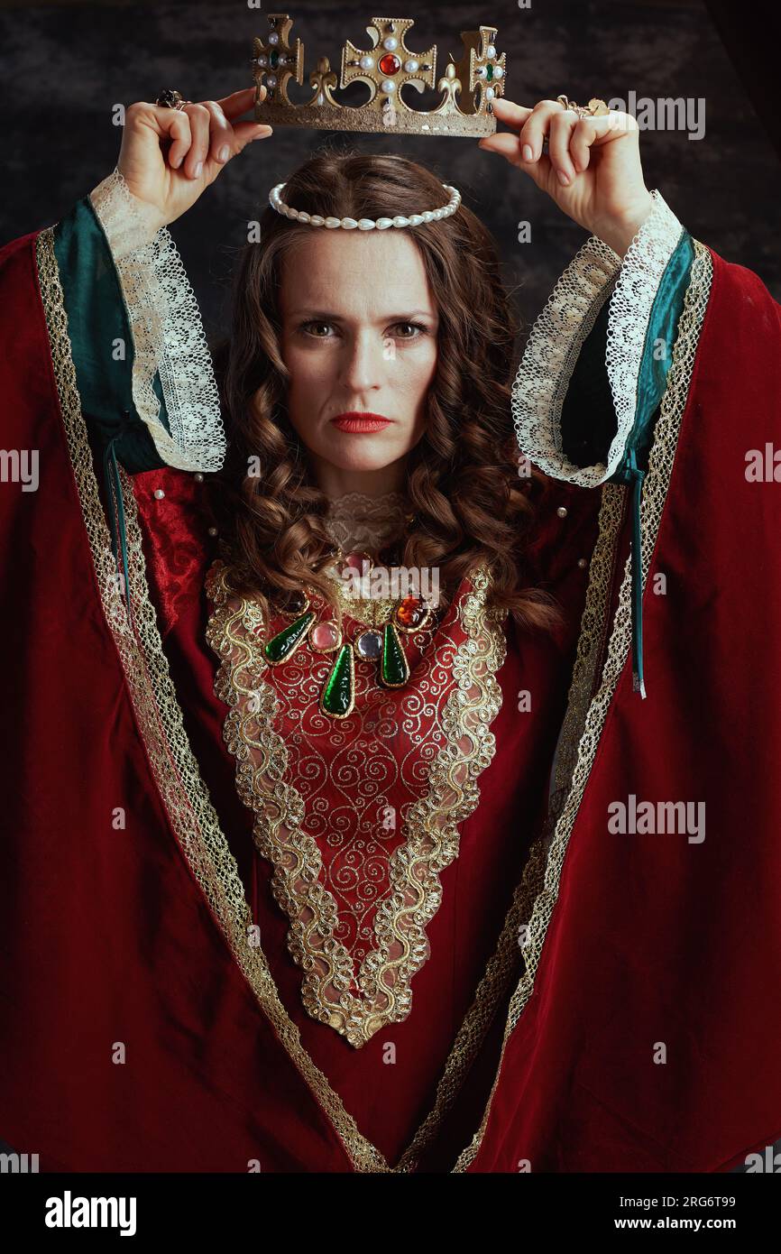 reine médiévale en robe rouge avec couronne sur fond gris foncé. Banque D'Images