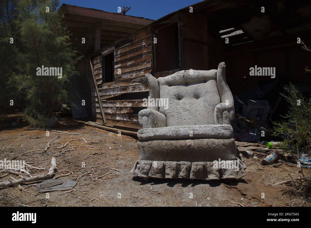 Canapé blanc vintage abandonné devant une cabane en bois abandonnée dans le désert à Salton Sea. Banque D'Images