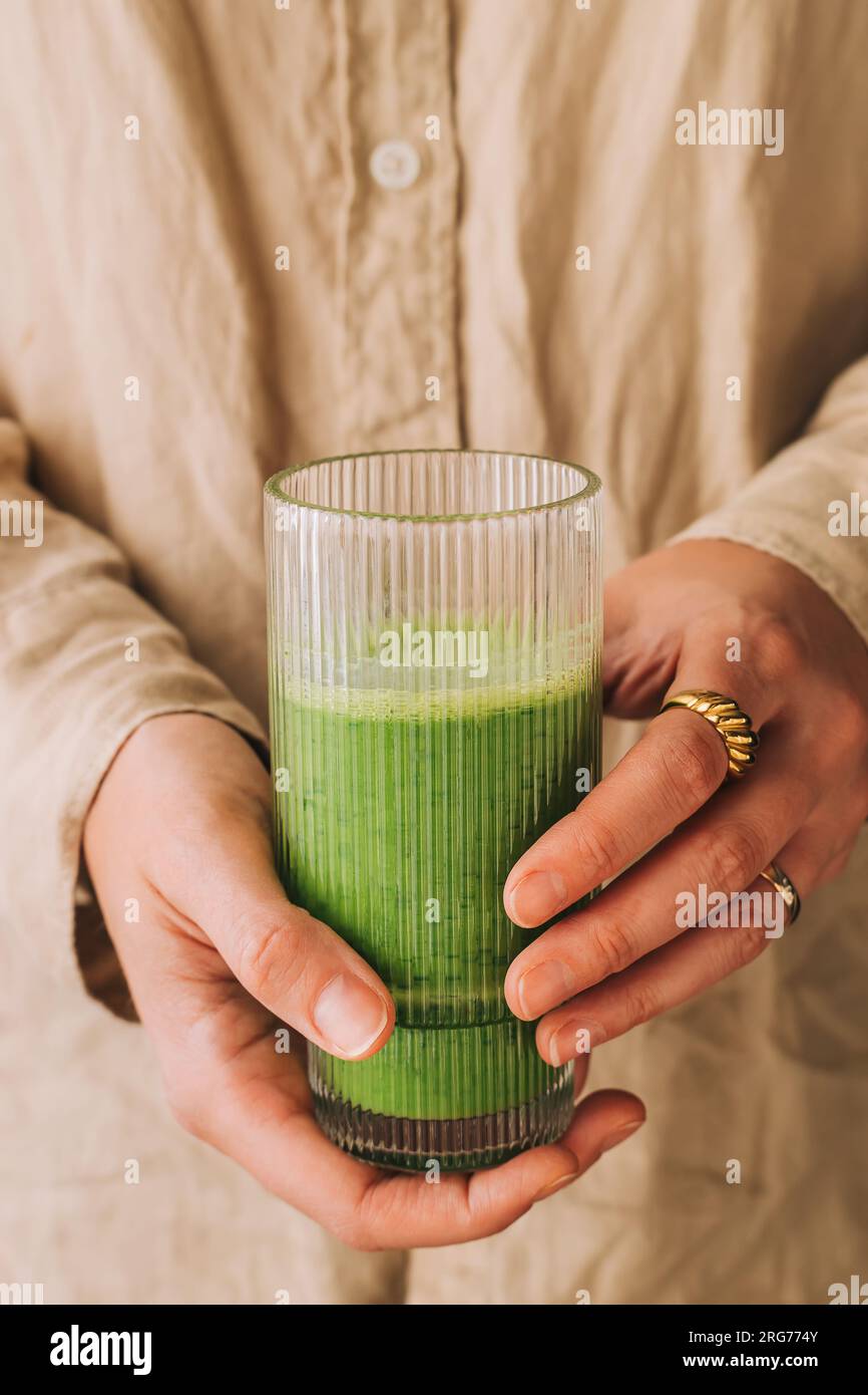 Gros plan des mains féminines tenant un verre avec un smoothie vert fraîchement mélangé, mode de vie sain Banque D'Images