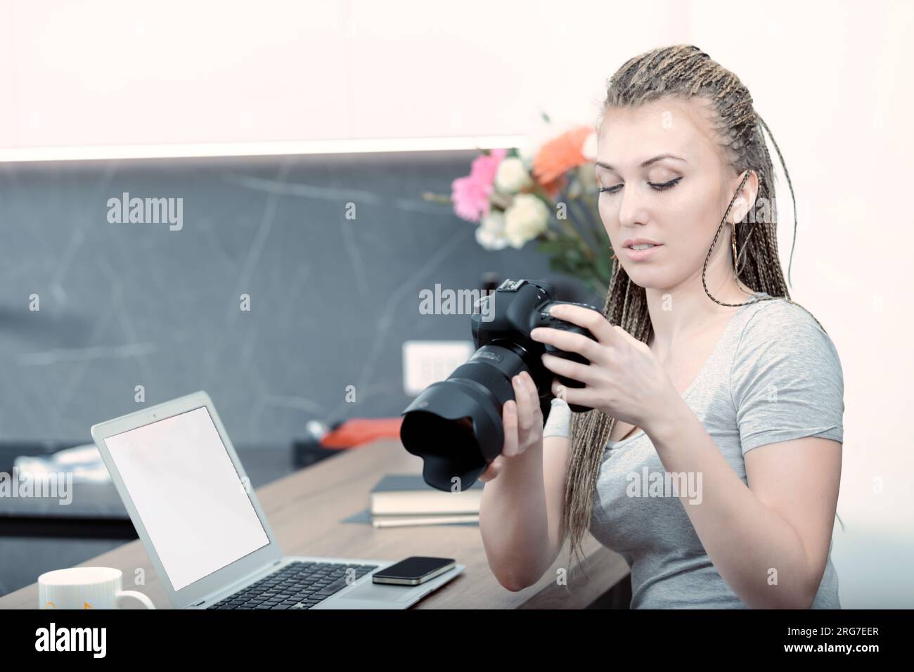 Une femme avec des cheveux en tresse de boîte, utilisant un reflex numérique et un ordinateur portable, cherche à comprendre son métier dans la cuisine, prête à obéir ou à enfreindre les règles Banque D'Images