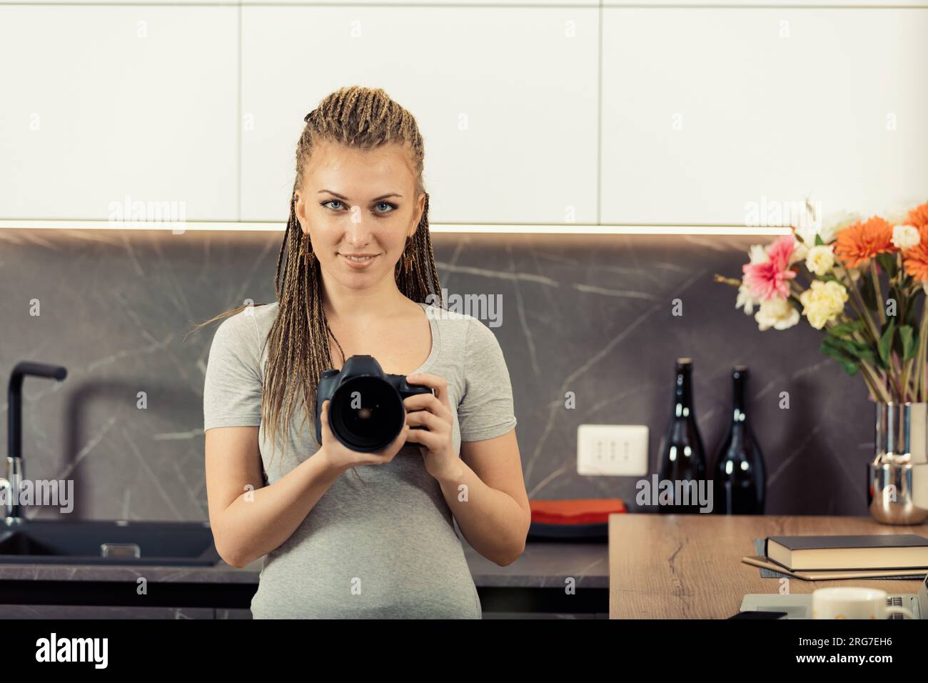 Jeune photographe avec des tresses en boîte plonge en profondeur à l'aide d'un reflex numérique et d'un ordinateur portable. Dans sa cuisine, elle teste les limites, connaissant les règles pour potentiellement les briser Banque D'Images