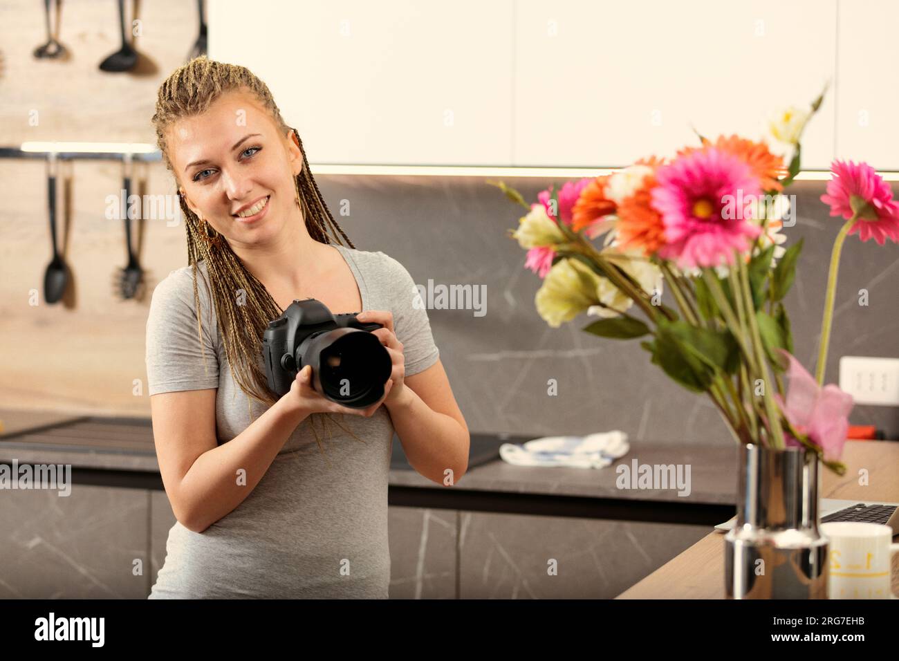 Femme tressée en boîte s'engage avec reflex numérique et ordinateur portable dans la cuisine. Sa quête : maîtriser la technique pour alimenter sa créativité Banque D'Images