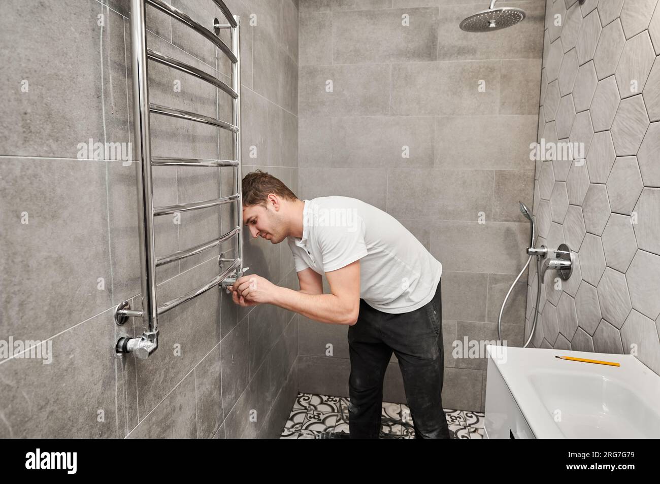 Homme accrochant un sèche-serviettes électrique sur le mur avec des  carreaux de céramique dans la salle de bains. Travailleur masculin  installant un chauffe-serviette de bain dans un appartement en rénovation.  Concept de