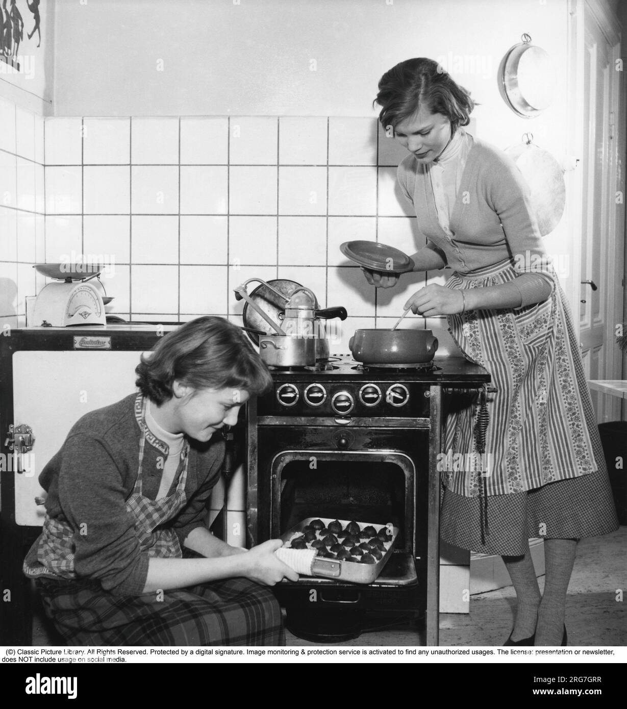 Dans la cuisine dans les années 1950 Deux jeunes femmes dans la petite cuisine cuisinant ensemble à la fois sur la cuisinière à gaz et dans le four. Suède 1955 Banque D'Images