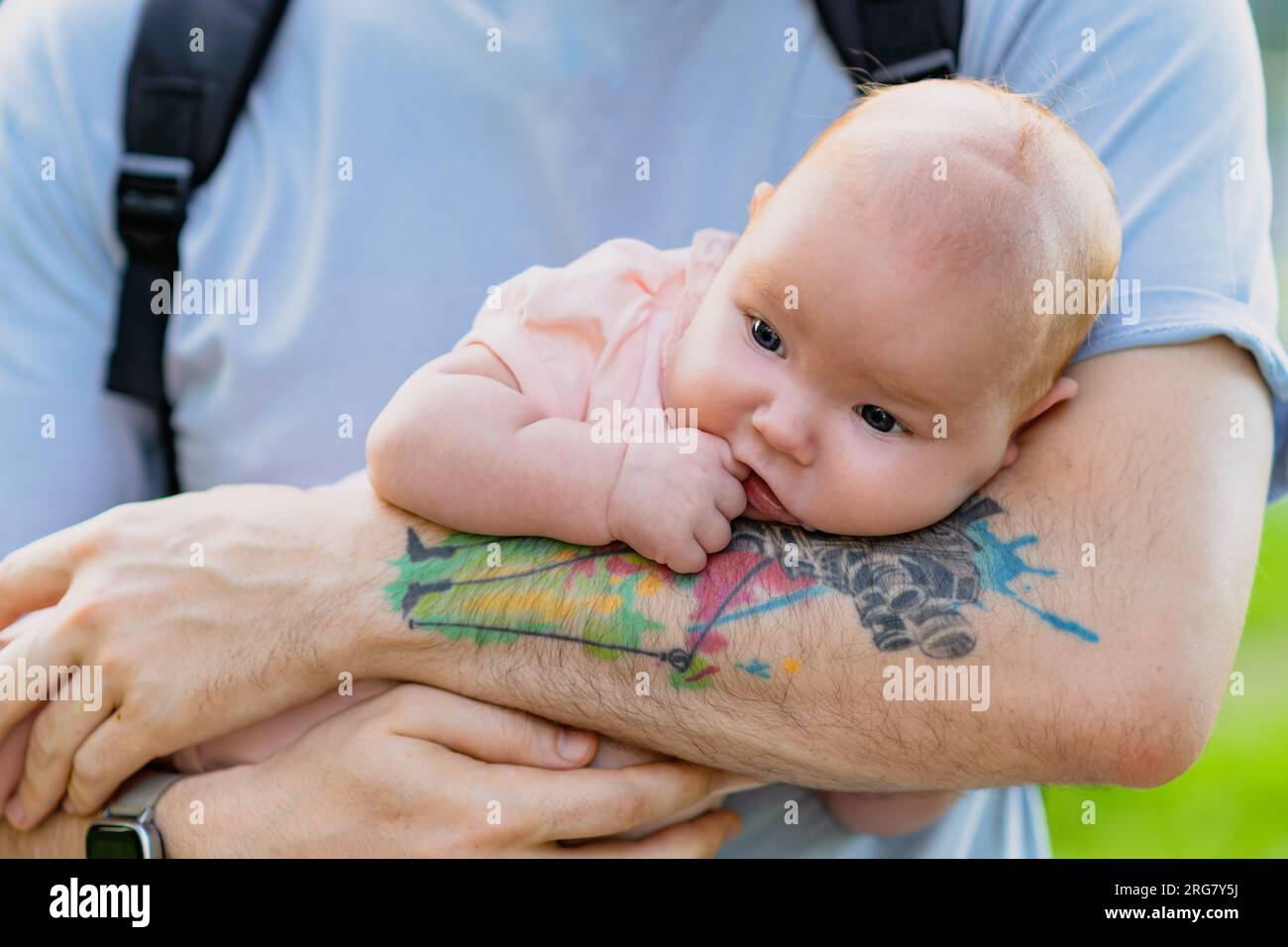 Un père avec un tatouage berce un nouveau-né tout en se tenant dans la rue. Banque D'Images