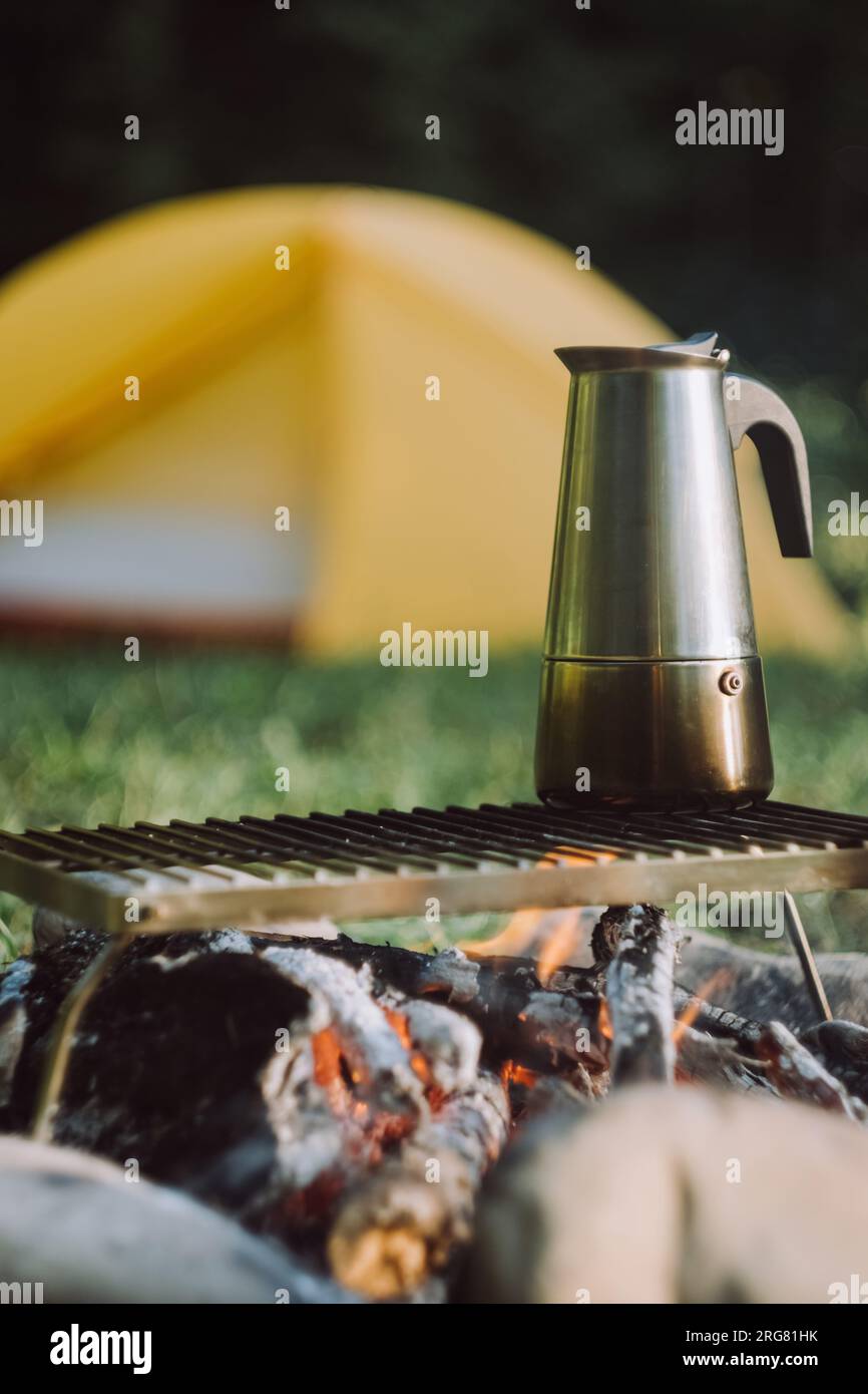 Foyer sélectif de café préparé dans geyser cafetière sur feu de camp le matin d'été. Boisson de petit-déjeuner pendant la randonnée. Feu de joie sur tente de fond et Banque D'Images