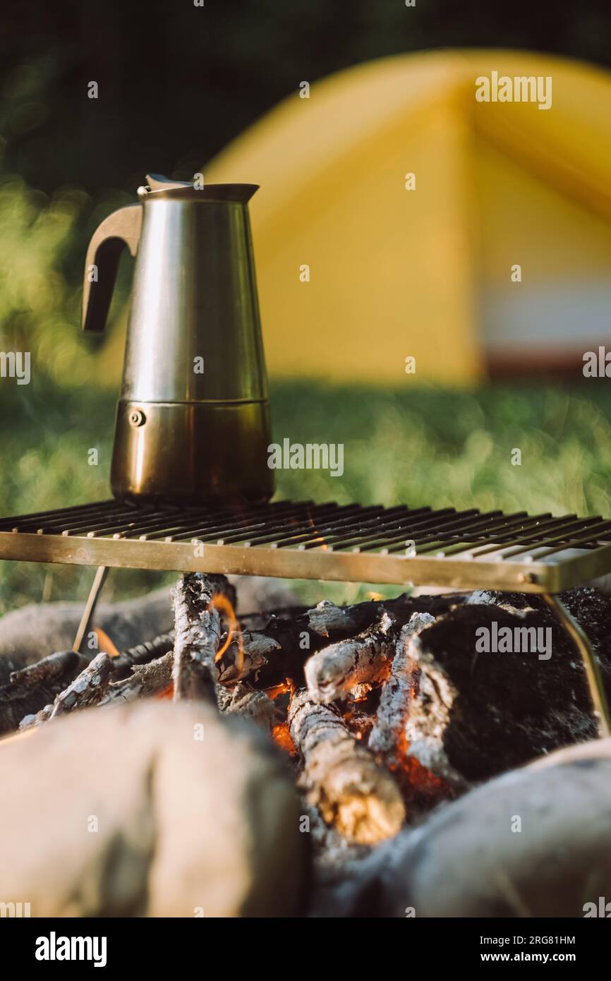 Gros plan de la cafetière geyser sur le feu de joie près de tente dans le parc d'été vert au lever ou au coucher du soleil. Ambiance de camping, nature et style de vie en plein air Banque D'Images