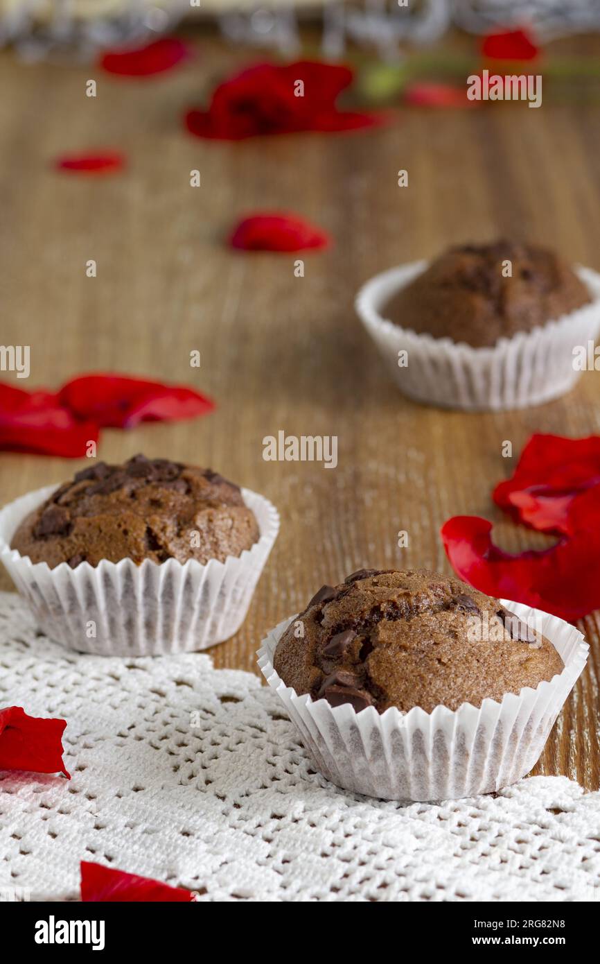 Gros plan de délicieuses natures mortes de cupcakes au chocolat noir faits à la maison, entourés de pétales de coquelicot rouge sur une table en bois rustique. Vue verticale. Bien Banque D'Images