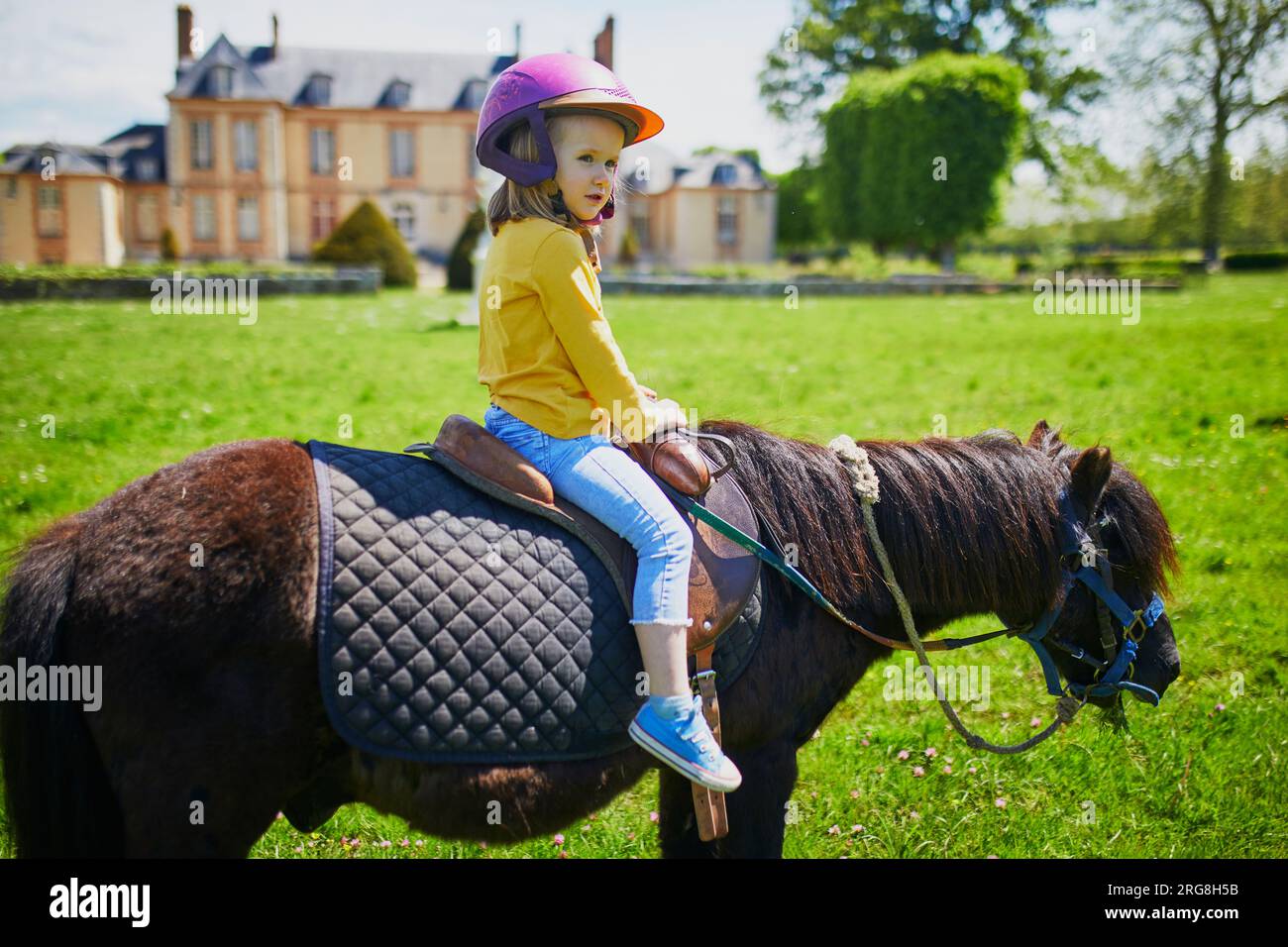 Adorable fille de trois ans chevauchant un poney. Petit enfant pratiquant l'équitation. Equestrianisme pour les petits enfants. Activités estivales en plein air pour chi Banque D'Images