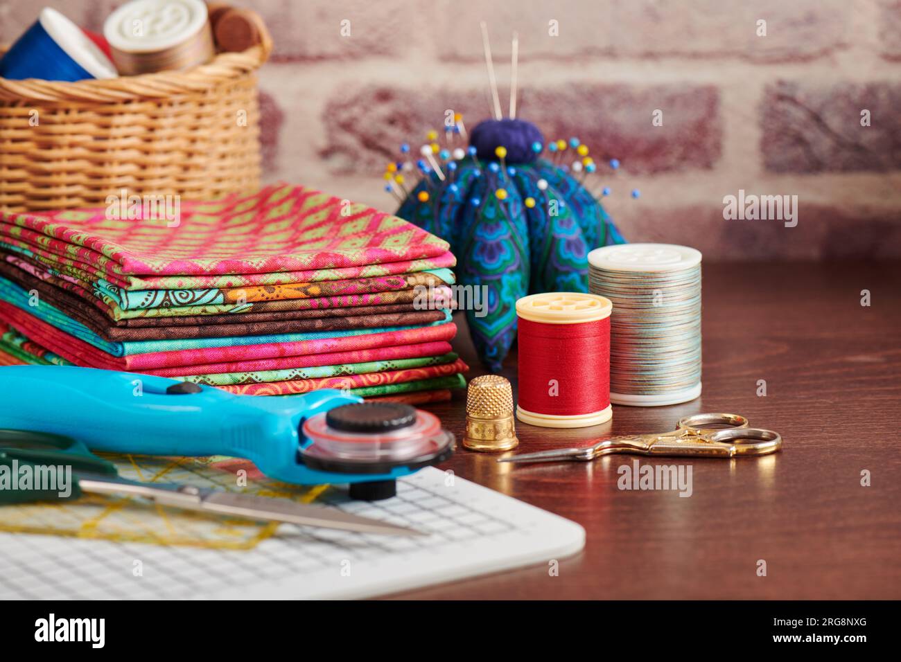 Pile de tissus colorés sur la table entourée d'accessoires de couture sur fond de mur en brique Banque D'Images