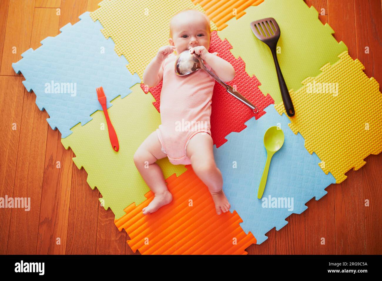 Bébé fille avec ustensiles de cuisine. Petit enfant allongé tapis de jeu et jouant avec les ustensiles de cuisine. De vraies choses comme des jouets pour les enfants. Enfant en bas âge dans nurser ensoleillé Banque D'Images