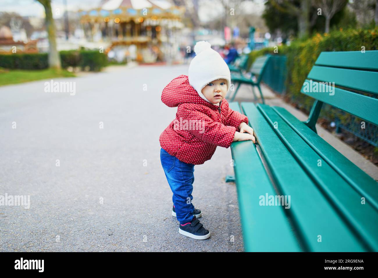 Petite fille debout dans la rue et tenant sur le banc. Petit enfant tirant vers le haut dehors Banque D'Images