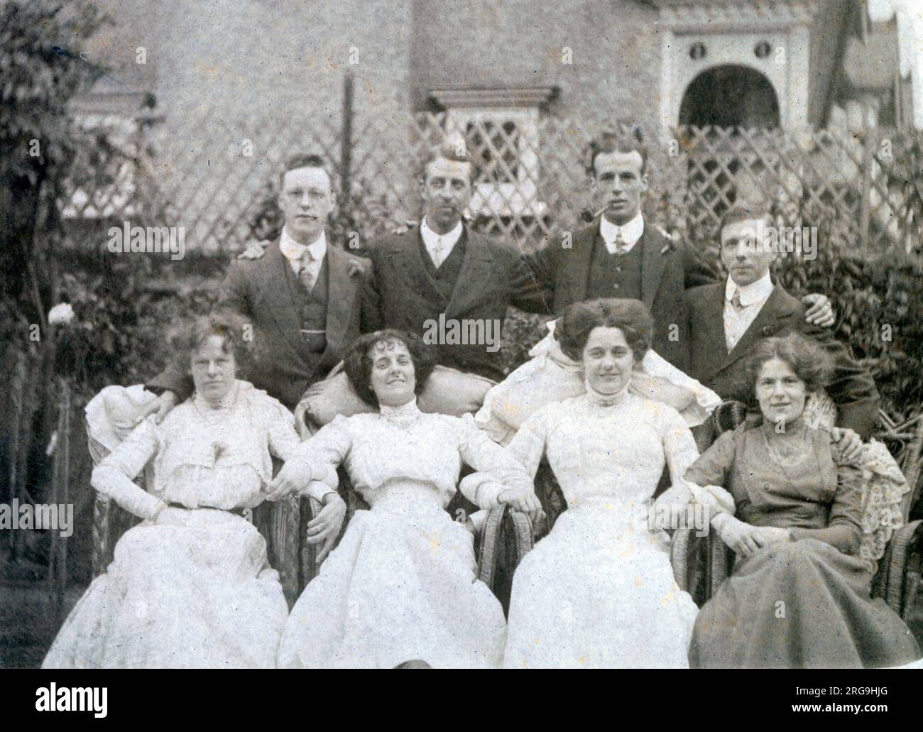 Quatre couples très habilement vêtus posent pour une photo de jovile dans un jardin de banlieue élégant. Banque D'Images