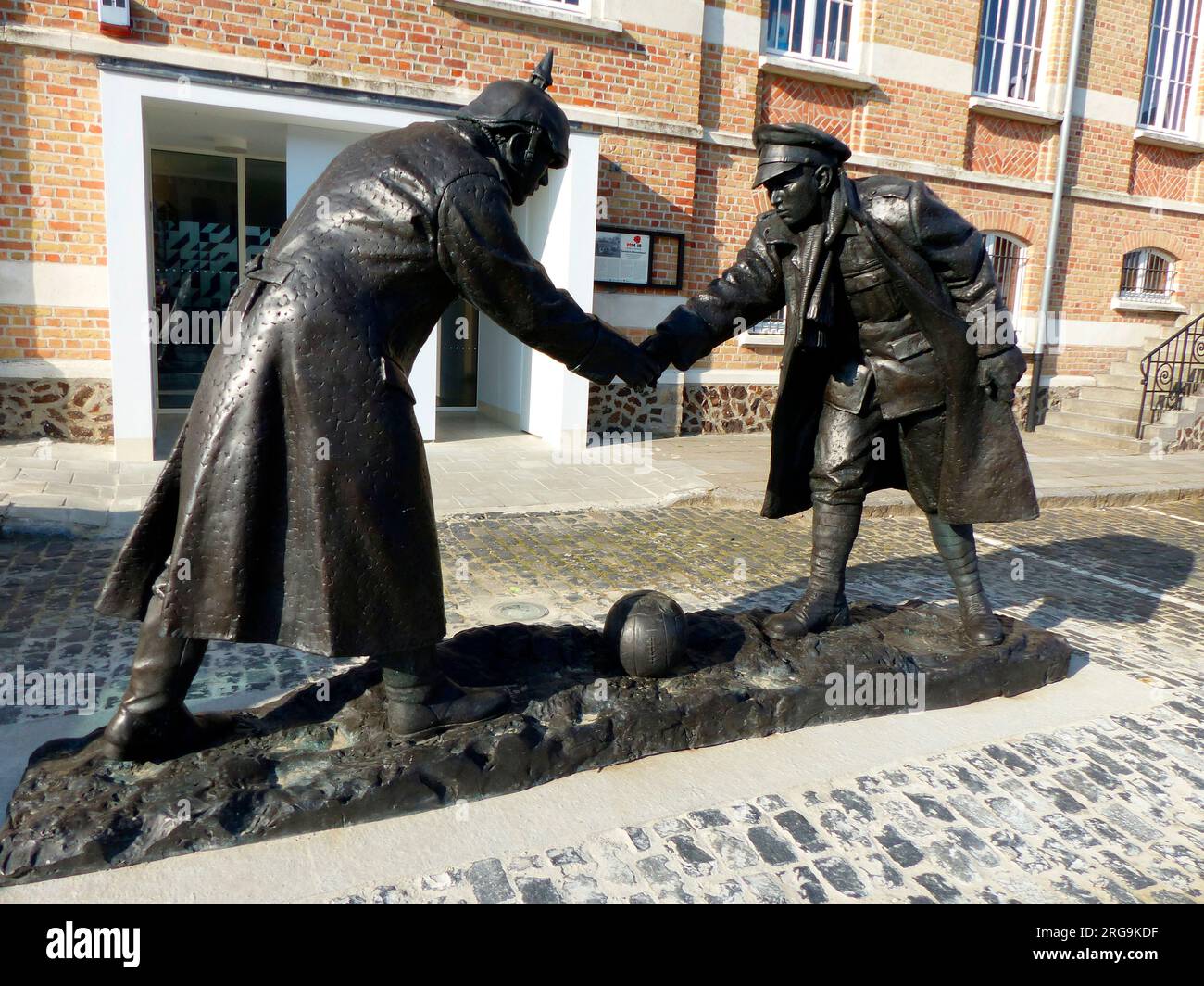 Cette statue grandeur nature d'un soldat allemand et britannique qui se secoue au-dessus d'un ballon de football, a été sculptée par Andy Edwards et a été dévoilée le 22 décembre 2015. Un match de football a eu lieu juste avant Noël 1914 mais, comme le titre du premier village à être libéré après le jour J en Normandie en 1944, il y a concurrence pour revendiquer la propriété de l'événement. Il est bien documenté qu'une trêve a eu lieu dans le village voisin de St Yvon et qu'un match de football a eu lieu à Frelinghien. Banque D'Images