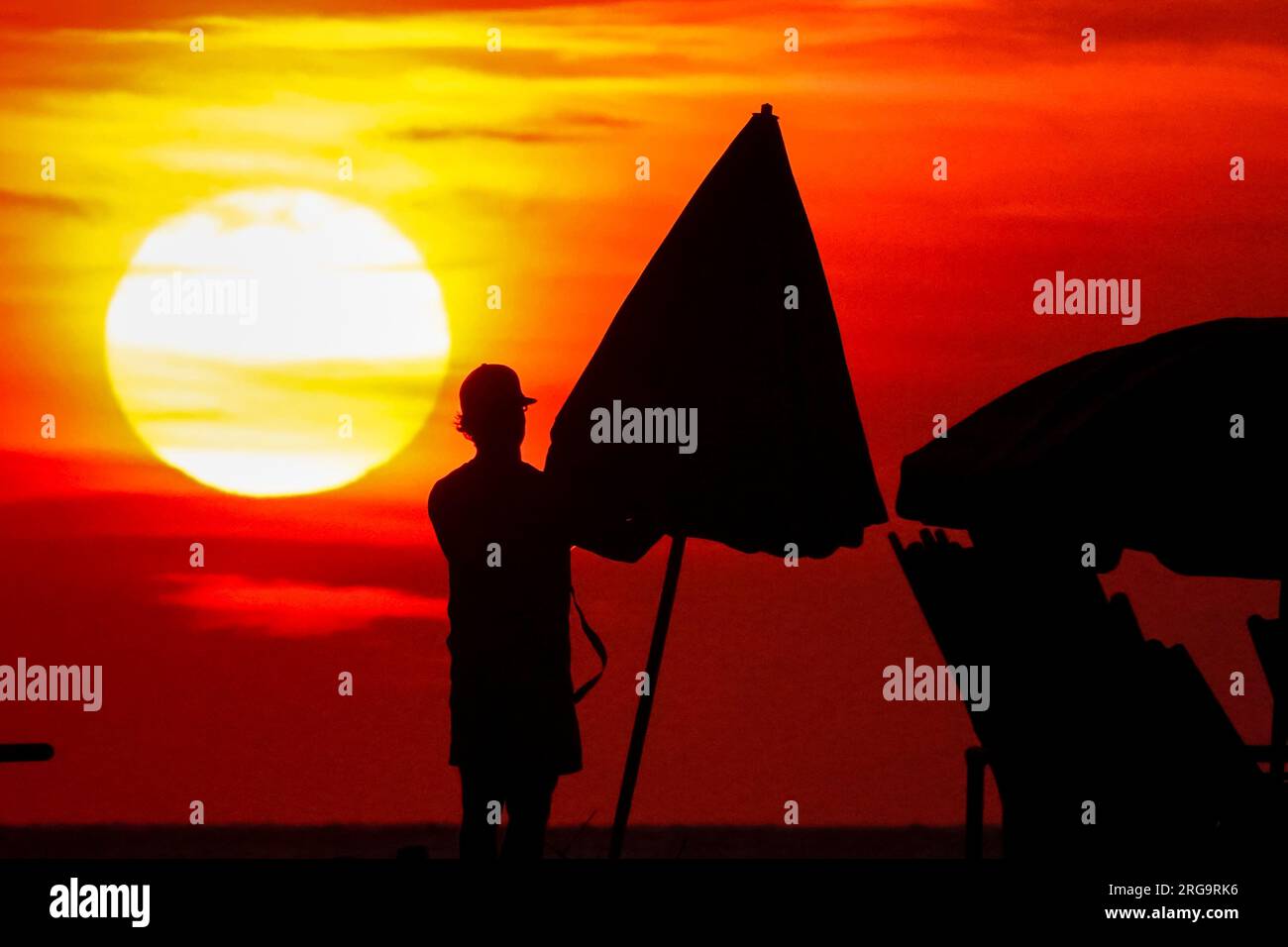 Île de Palms, États-Unis. 08 août 2023. Un employé de la station ouvre un parasol alors que le soleil se lève sur la plage lors d'une journée record chaude et humide dans la région de Charleston, le 8 août 2023 à Isle of Palms, Caroline du Sud. Une vague de chaleur persistante dans le sud des États-Unis continue d'apporter un temps extrêmement chaud et humide à la région. Crédit : Richard Ellis/Richard Ellis/Alamy Live News Banque D'Images