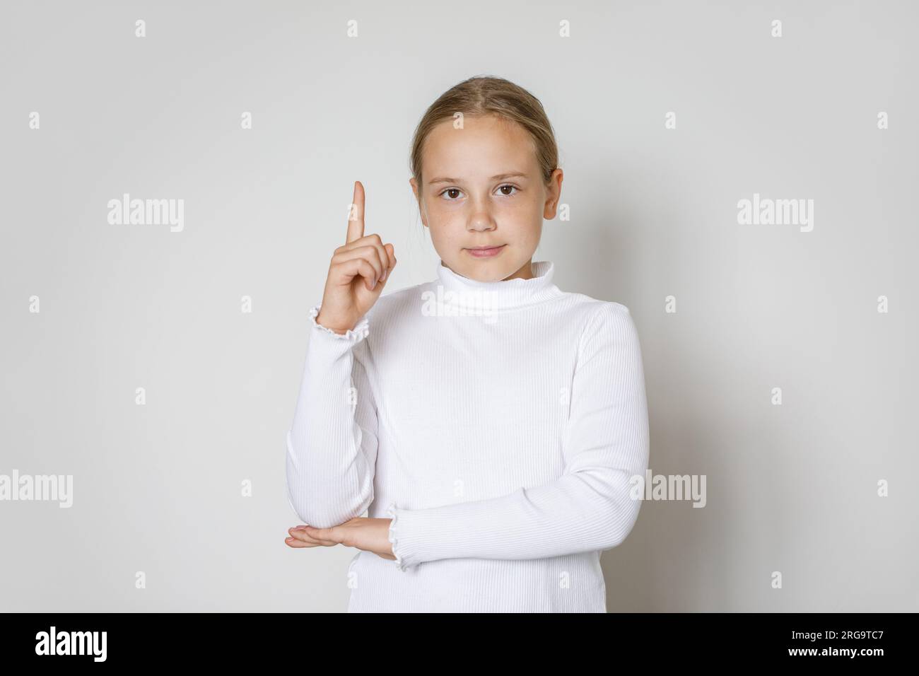 Portrait d'une petite fille joyeuse pointant du doigt vers le haut contre le fond blanc du mur de studio. Kid 10 ans Banque D'Images