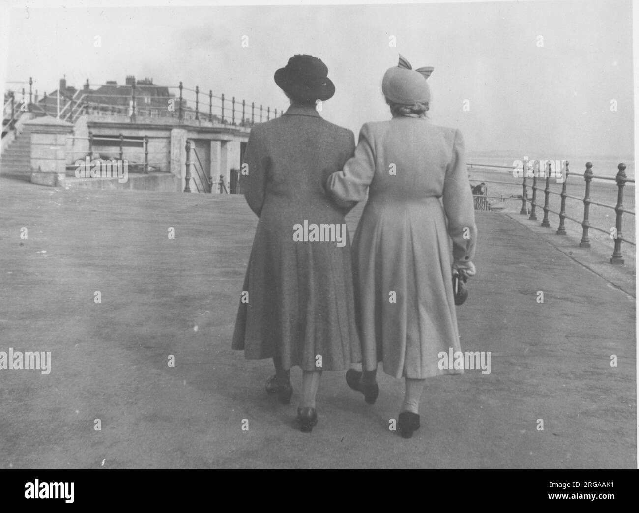 Vue arrière de deux dames marchant le long d'un front de mer non identifié bras dans bras. Banque D'Images