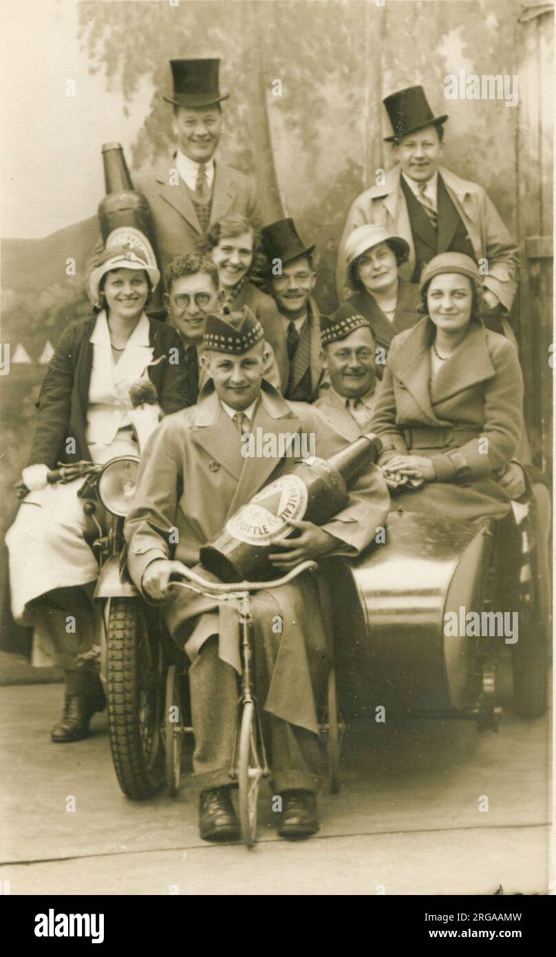 Un groupe joyeux de vacanciers pose pour une photographie avec une bouteille de bière prop, divers modes de transport et des chapeaux dans un studio Blackpool. Banque D'Images