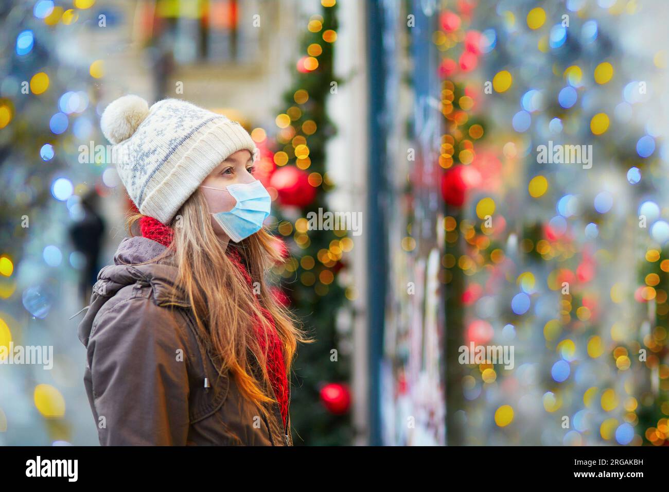 Fille portant un masque facial dans une rue parisienne ou au marché de Noël regardant les vitrines décorées pour Noël. Vacances saisonnières pendant la pandémie Banque D'Images