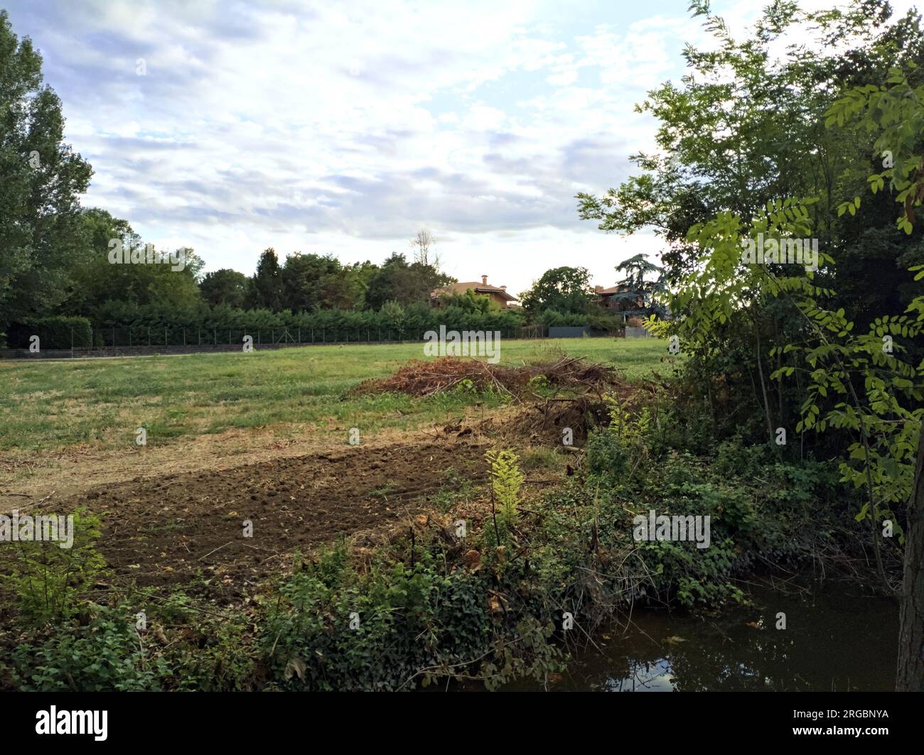 Champ et maisons bordés par une tranchée avec eau et arbres au coucher ...