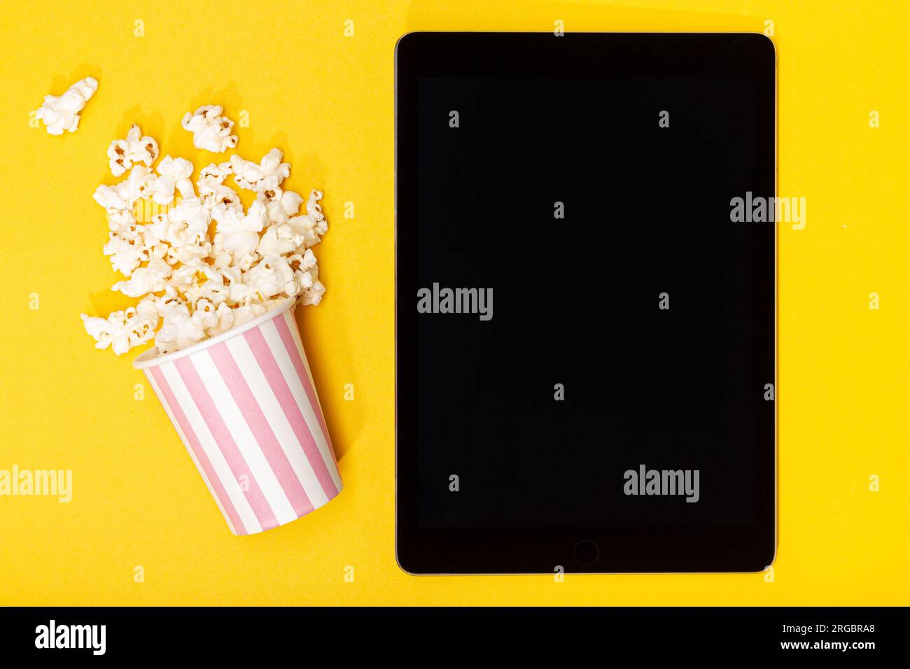 Seau à pop-corn et tablette à écran noir vierge sur fond jaune. Vue de dessus Banque D'Images