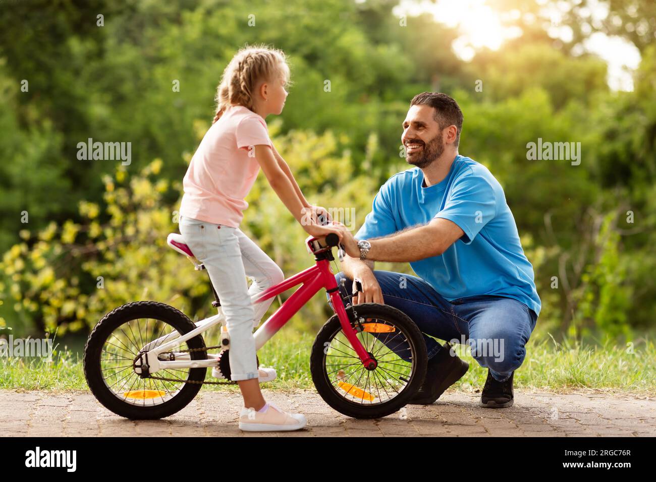 Des valeurs familiales heureuses. Vue latérale du beau père d'âge moyen et sa fille marchant avec le vélo dans le parc vert et parlant Banque D'Images