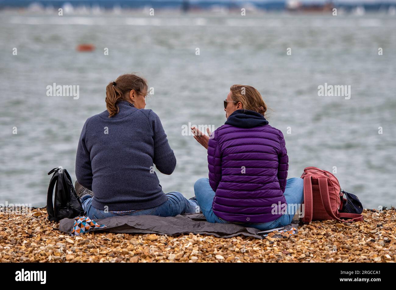 deux dames plus âgées assis ensemble sur une plage de galets bavardant et passant le temps partagé ensemble Banque D'Images