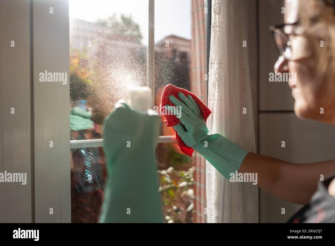 Femme versant un spray liquide sur le verre pour le nettoyer avec un chiffon. Banque D'Images