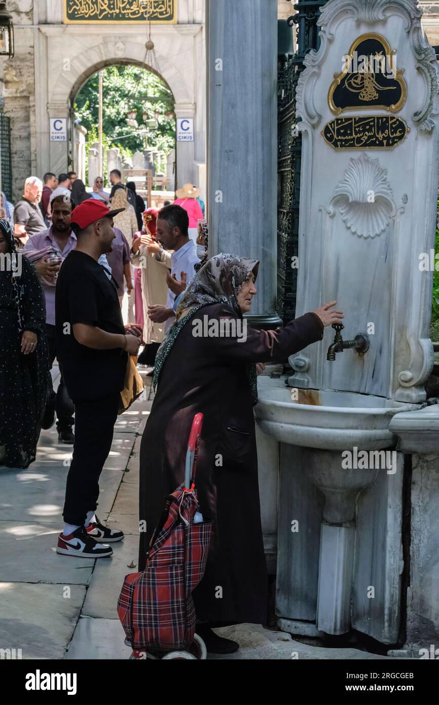 Istanbul, Turquie, Türkiye. Femme obtenant de l'eau à un robinet dans la cour de la mosquée Eyup Sultan, Banque D'Images