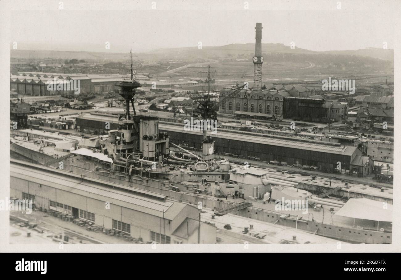 Rosyth Royal Naval Dockyard - Fife, Écosse - vue panoramique montrant la centrale électrique et la cheminée industrielle avec plusieurs cadrans d'horloge. Au premier plan se trouve un cuirassé de la classe Revenge, probablement le HMS Resolution, montrant la plate-forme de l'avion sur la tourelle du canon. Banque D'Images