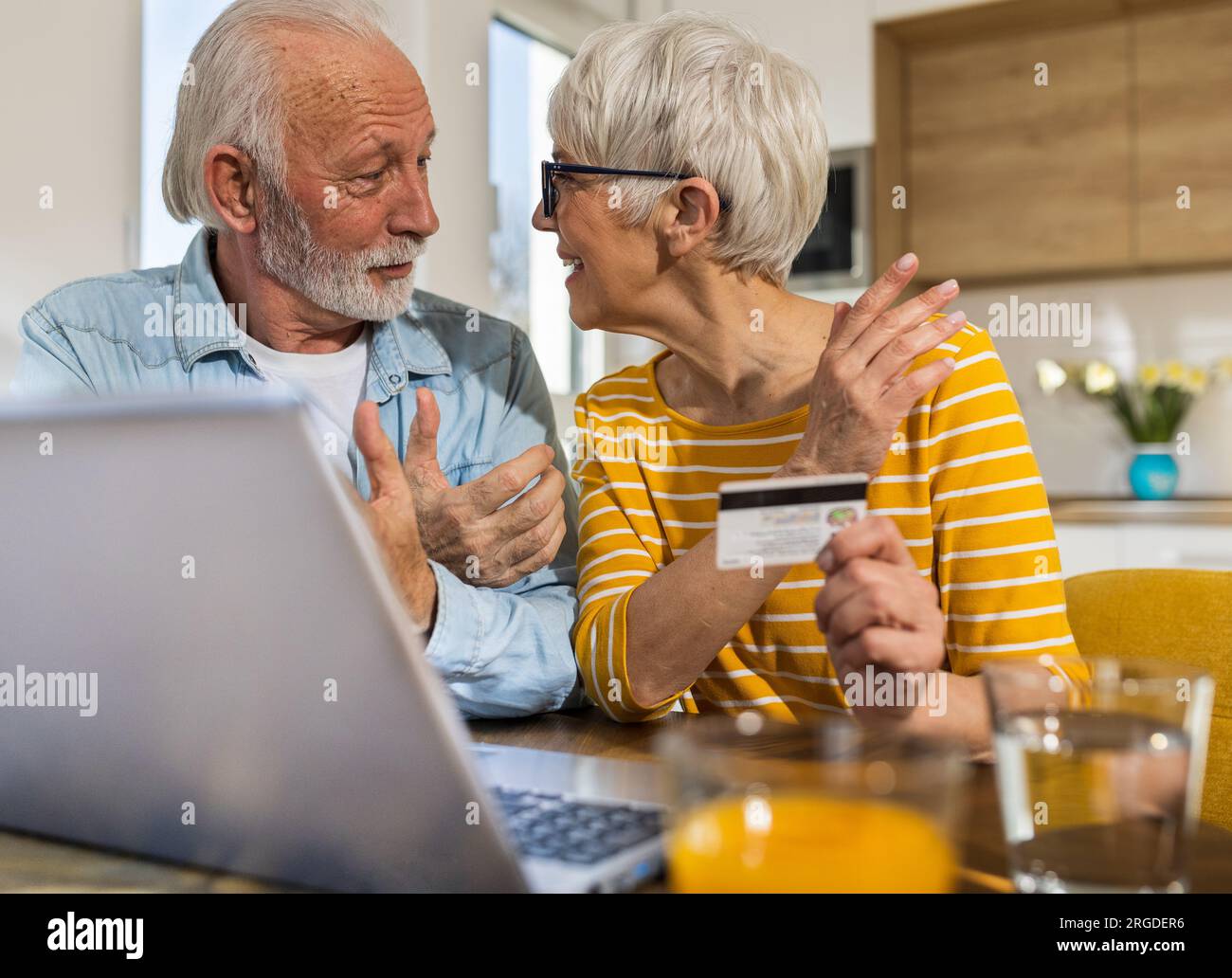 Joyeux couple senior assis à la table de salle à manger avec cuisine en arrière-plan et acheter en ligne avec carte de crédit Banque D'Images