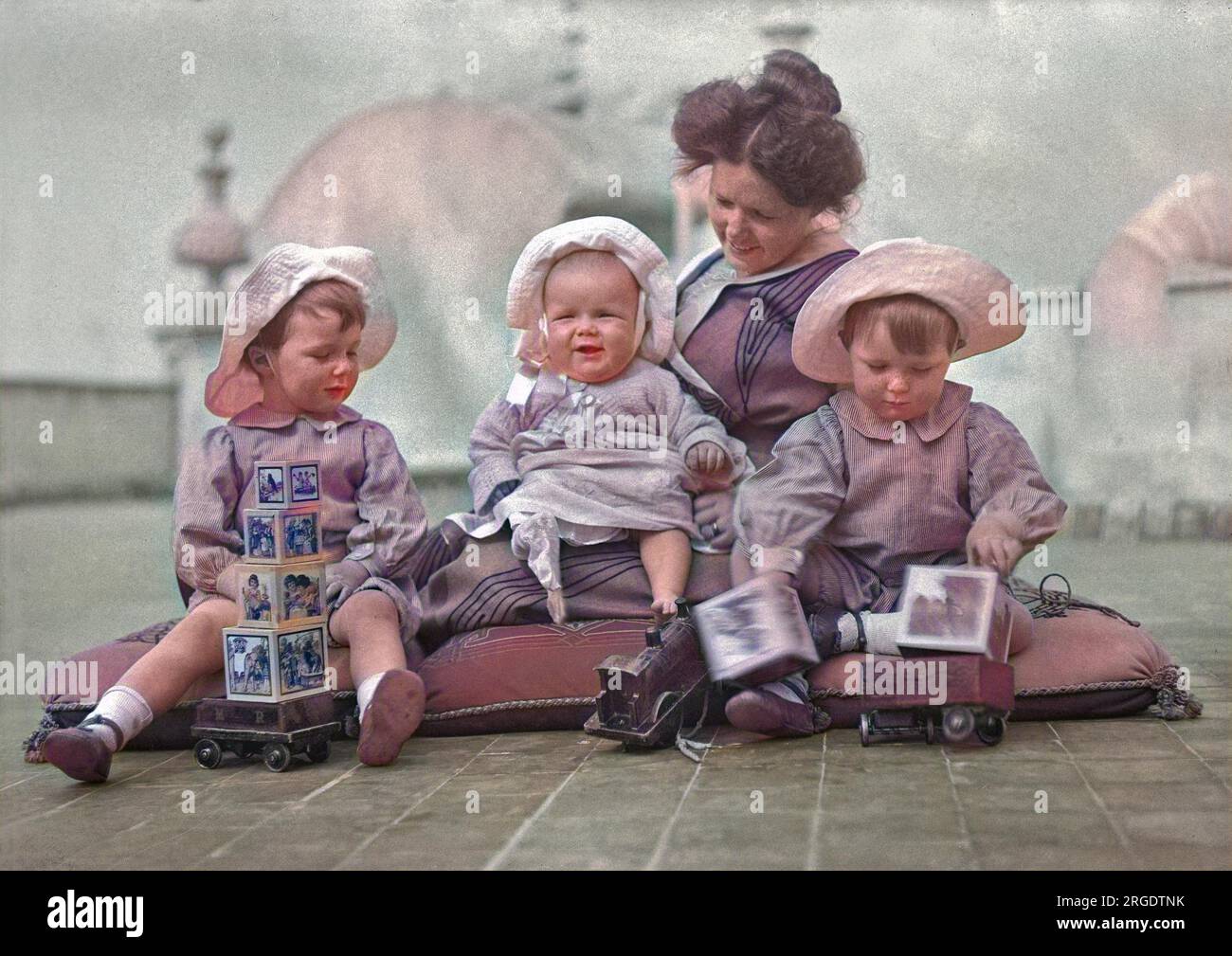 Une mère et ses trois enfants assis sur des coussins au sol avec des blocs de construction et des trains de jouets. Banque D'Images