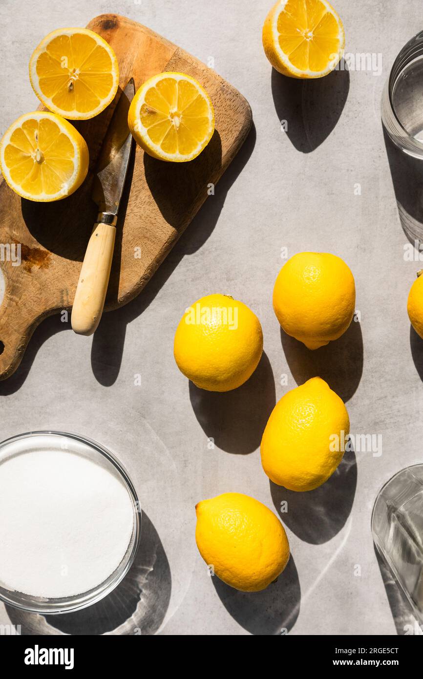 Citrons à la lumière dure, avec du sucre, de l'eau et des citrons tranchés autour. Banque D'Images