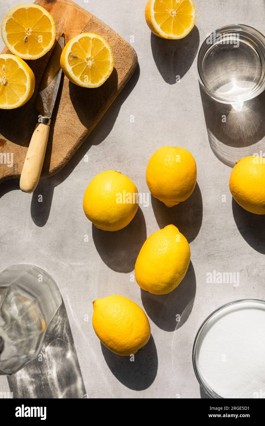 Citrons à la lumière dure, avec du sucre, de l'eau et des citrons tranchés autour. Banque D'Images