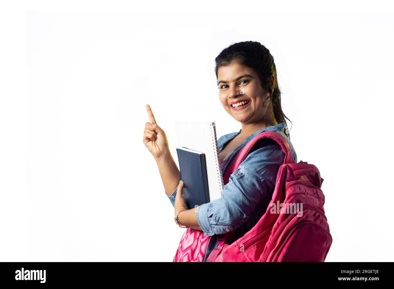 Une jolie jeune fille indienne avec des livres à la main et sac à dos pointant avec le visage souriant sur fond blanc Banque D'Images