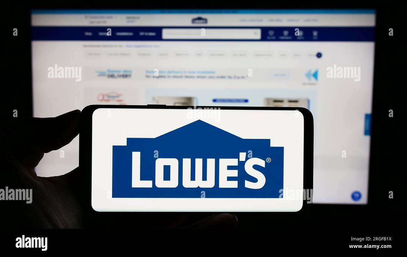 Personne détenant un téléphone cellulaire avec le logo de la société de détail américaine Lowe's Companies Inc. À l'écran devant la page Web de l'entreprise. Concentrez-vous sur l'affichage du téléphone. Banque D'Images