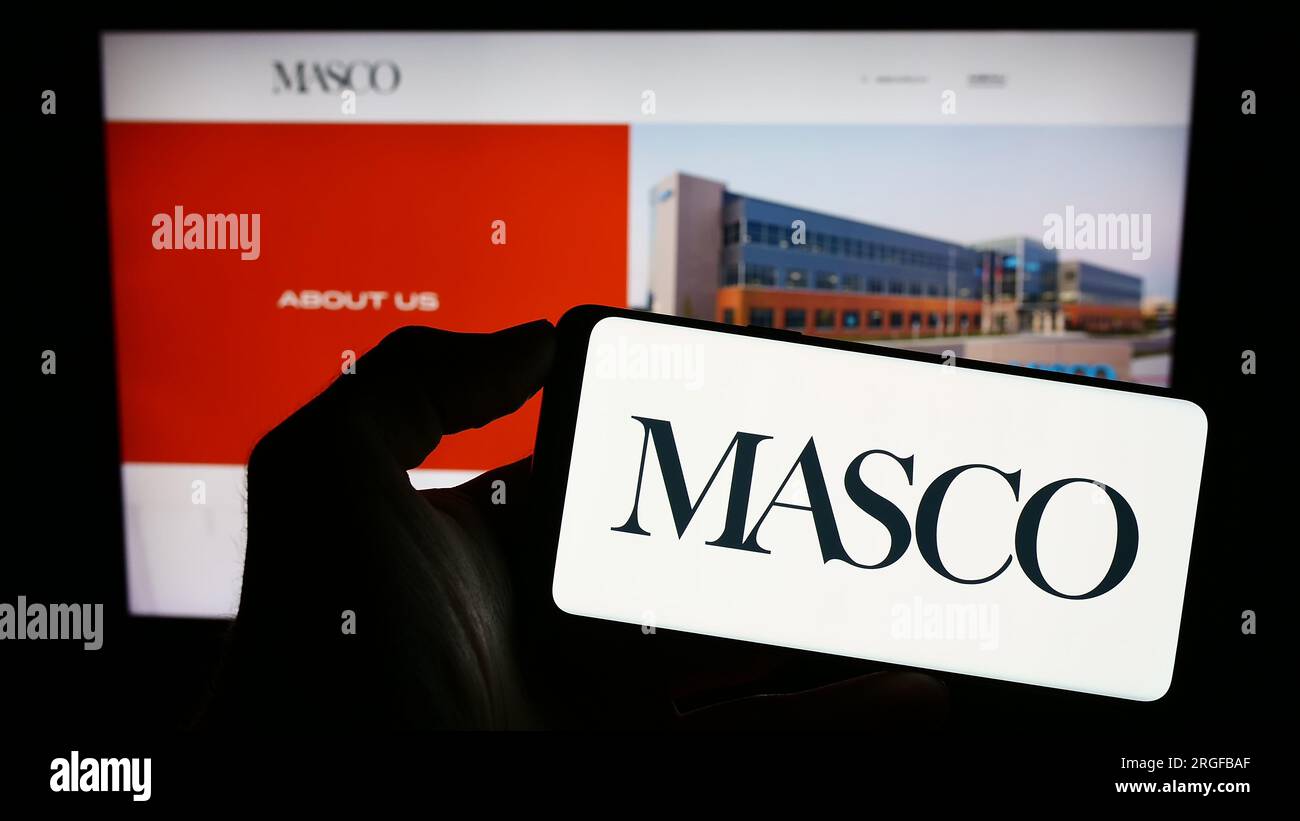 Personne tenant le téléphone portable avec le logo de la société américaine d'amélioration de la maison Masco Corporation sur l'écran en face de la page Web. Concentrez-vous sur l'affichage du téléphone. Banque D'Images