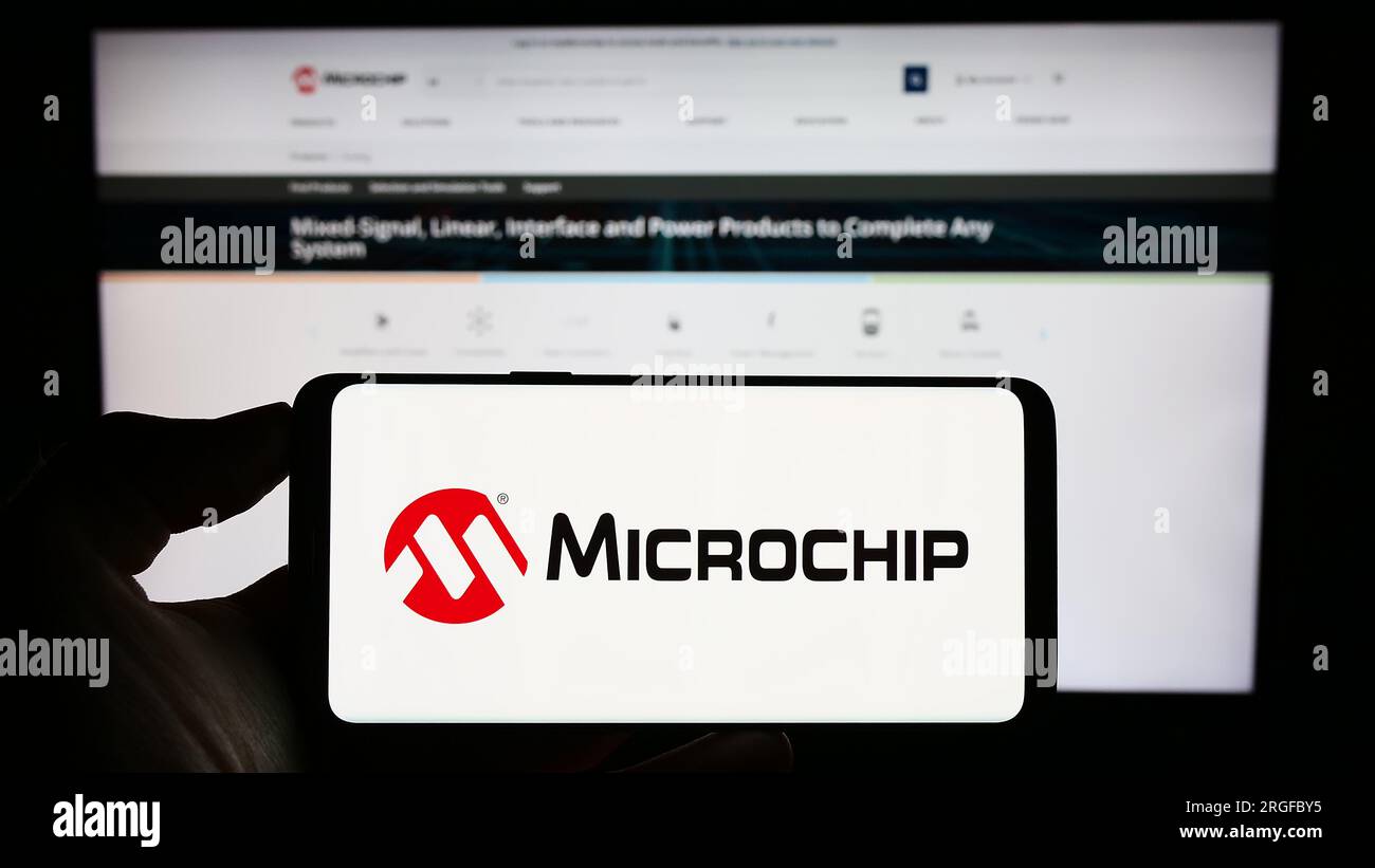 Personne tenant le téléphone cellulaire avec le logo de la société de semi-conducteurs Microchip Technology Inc. Sur l'écran devant la page Web. Concentrez-vous sur l'affichage du téléphone. Banque D'Images