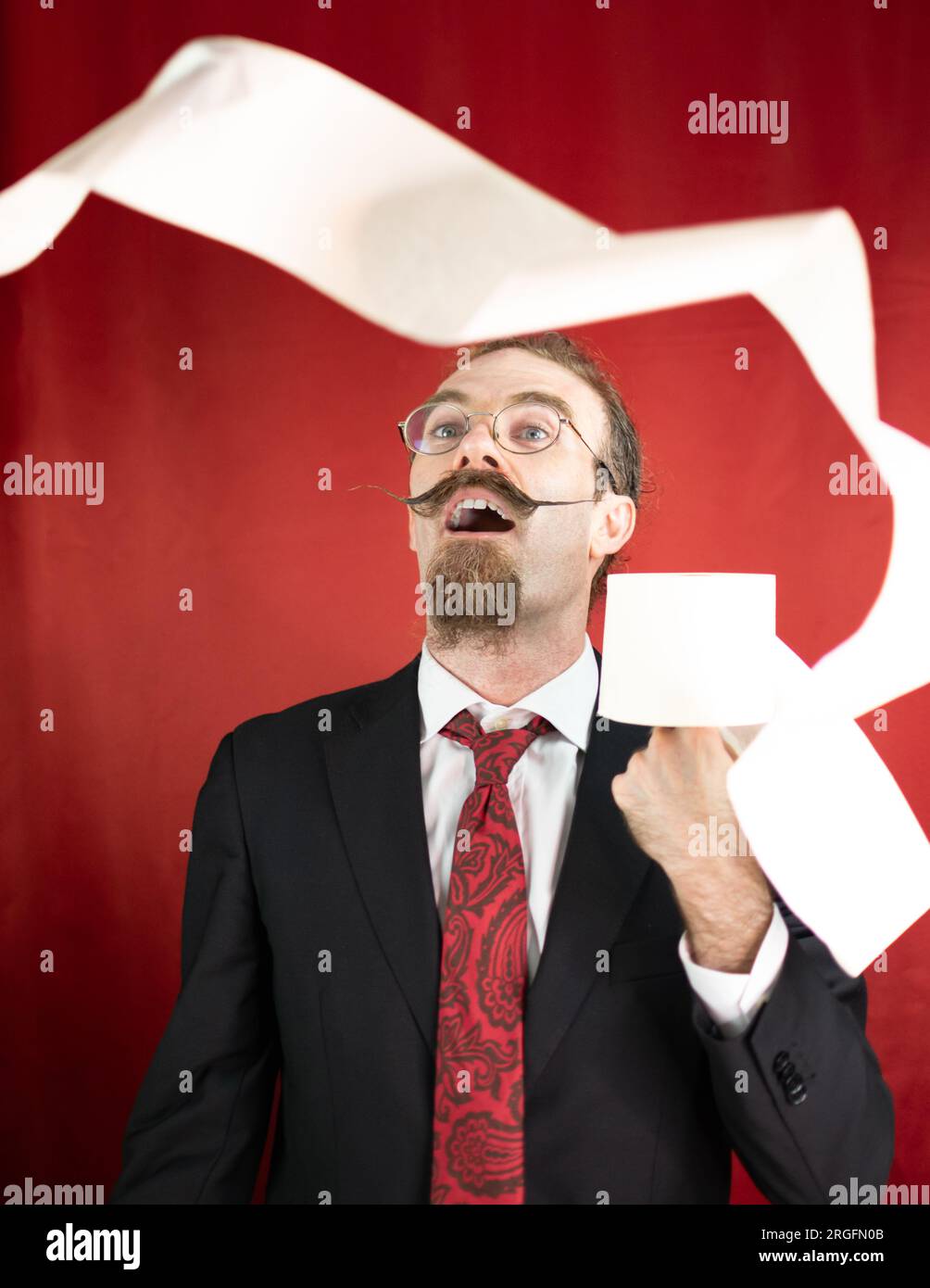 Homme choqué avec des lunettes, cravate rouge et papier toilette à la main regardant comment il vole Banque D'Images